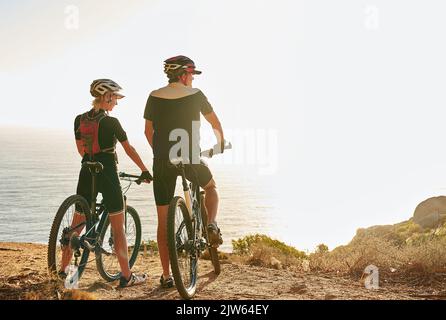 Accettate sempre un invito a cavalcare: Una giovane coppia che ammirerà il panorama dalla cima di una collina mentre fate un giro in bicicletta. Foto Stock
