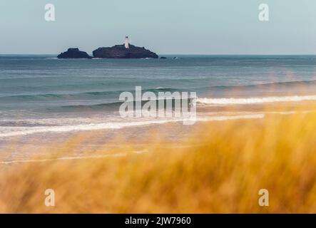 Le erbe dorate delle dune che soffiano nel vento mentre un racchetta naviga l'onda sulla spiaggia di Godrevy con il faro sul retro. Foto Stock