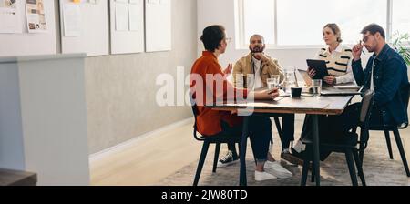 Gruppo di imprenditori creativi che hanno una discussione durante una riunione in un ufficio. Progettisti diversi che condividono idee mentre lavorano insieme su una nuova de Foto Stock