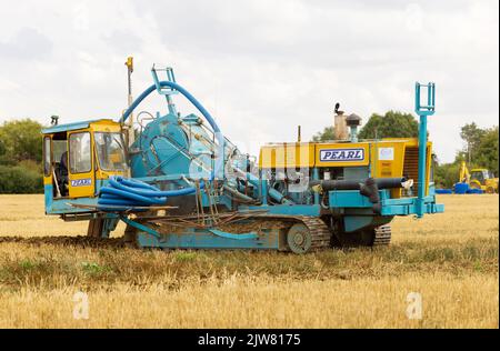 Macchina per lo scavo di trincee che lavora in un campo scavando un canale di drenaggio e posando un tubo di drenaggio del terreno. REGNO UNITO Foto Stock