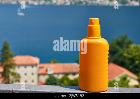 Bottiglia arancione di una crema solare spray con un mare sullo sfondo Foto Stock