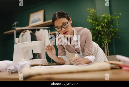 Giovane stilista di moda femminile che lavora sui suoi disegni di abito in studio. Donna che lavora in studio di moda. Foto Stock