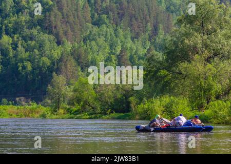 Un gruppo di turisti è rafting su un catamarano gonfiabile lungo il fiume tra alte rocce Foto Stock