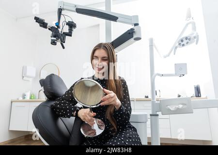 Giovane donna che guarda nello specchio dopo una procedura dentale Foto Stock