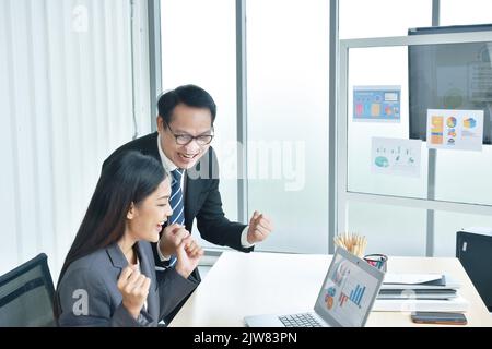 Felice uomo e donna asiatico busimess guardando lo schermo del notebook con il momento di successo in ufficio Foto Stock