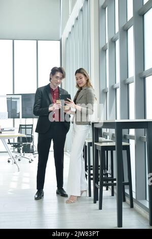 Felice uomo e donna asiatico busimess guardando il telefono cellulare per rilassarsi dopo il lavoro in ufficio Foto Stock