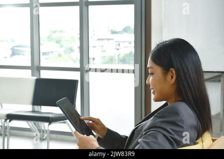 Felice donna asiatica senza busimess che guarda il telefono cellulare per rilassarsi dopo il lavoro in ufficio Foto Stock