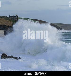 Onde massicce che battono sulla spiaggia di Porthleven con Tye Rock Manor appollaiato sulla scogliera dietro. Foto Stock