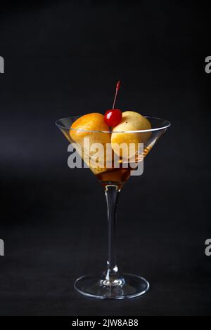 Rum baba napoletano (o baba au rum) in un bicchiere di martini con una ciliegina da cocktail su sfondo nero. Piccole torte di lievito imbevute di sciroppo di rum. Tradizione Foto Stock