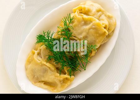 Gnocchi asiatici fritti Gyozas o gnocchi russi, ucraini, cerotti in piatto di ceramica bianca servito con panna acida. Primo piano. Cena asiatica. Giacitura piatta. Sfondo isolato bianco. Copia spazio. Foto Stock