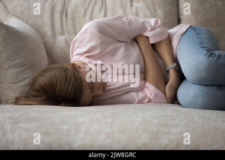 Giovane donna depressa e malata sdraiata sul divano in posizione embrionale Foto Stock