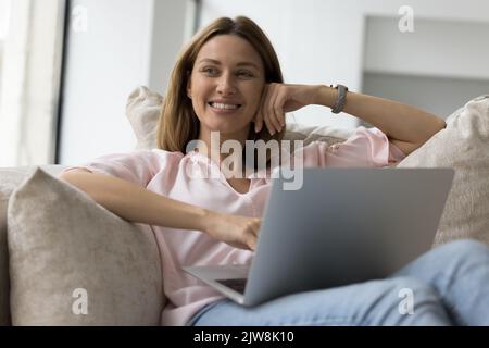 Felice utente di un notebook che si rilassa a casa, riposandosi su un divano morbido Foto Stock