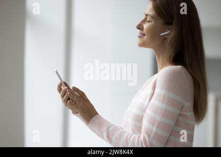Donna allegra e tranquilla con cuffie wireless all'orecchio Foto Stock