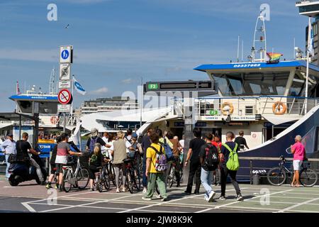 Amsterdam, Paesi Bassi - 2022 agosto: Folla di persone e ciclisti che catturano un traghetto fluviale dal centro della città Foto Stock