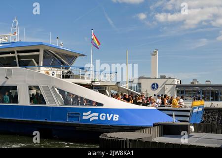 Amsterdam, Paesi Bassi - 2022 agosto: Traghetto fluviale in arrivo sul lungomare con una folla di persone sul ponte Foto Stock