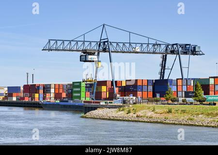 Rotterdam, Paesi Bassi - Agosto 2022: Grande gru mobile che solleva un container da una chiatta industriale sul fiume vicino Rotterdam Foto Stock