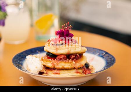 Appetitose frittelle decorate con frutti di bosco e fiori. Foto Stock