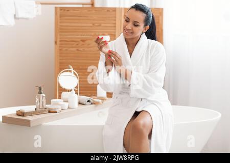 Misto femmina Holding vaso idratante idratante mani seduta in bagno Foto Stock
