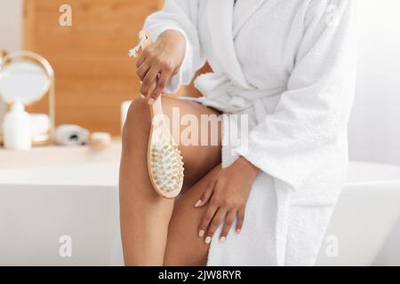 Massaggio Lady Making Legs con spazzola di legno in bagno, tagliato Foto Stock