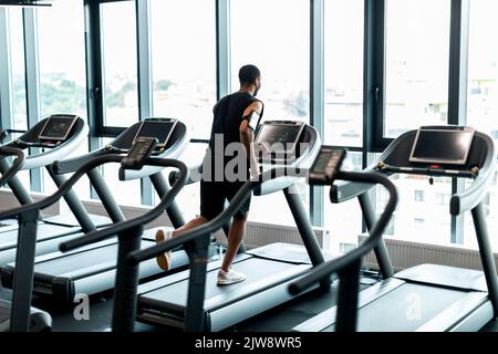 Allenamento cardio. Black Man che corre sul tapis roulant vicino alla finestra panoramica della palestra Foto Stock