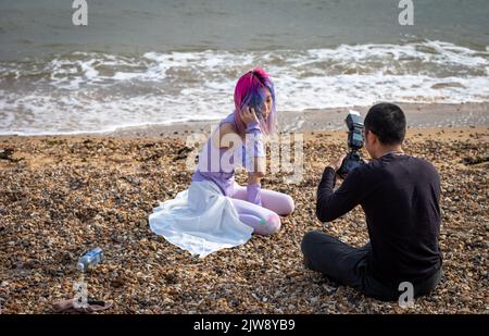 Un giovane uomo asiatico scatta foto della sua ragazza asiatica vestita con colori vivaci sulla spiaggia di Southend-on-Sea, Essex, Regno Unito. Foto Stock
