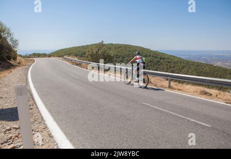 Ciclista senior che accelera la strada tortuosa CC-139. Scatto a basso movimento Foto Stock