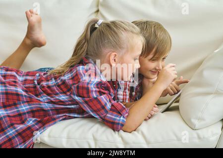 fratello e sorella sorridenti con un tablet sul divano in soggiorno Foto Stock