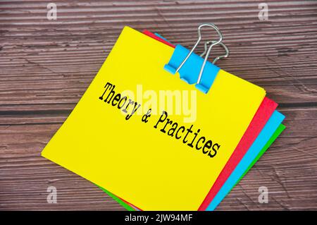 Testo di teoria e pratica su blocco note giallo con sfondo di legno della scrivania. Concetto aziendale. Foto Stock
