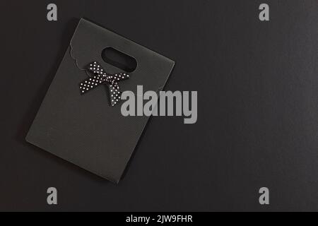 Busta regalo nera con fiocco a pois isolato su sfondo scuro. Su un lato è presente uno spazio vuoto. Foto Stock