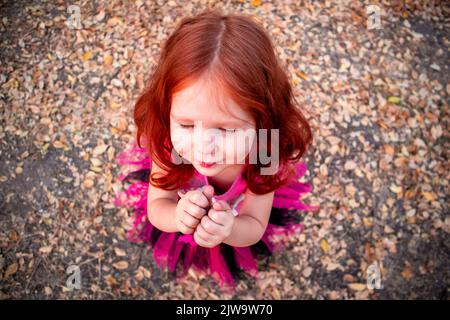 una bambina dai capelli rossi si alza con gli occhi chiusi vista dall'alto tra foglie gialle autunnali Foto Stock