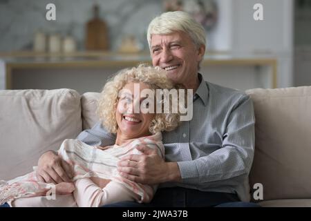 Felice sognante pensionato coppia di mezza età rilassarsi sul divano di casa Foto Stock