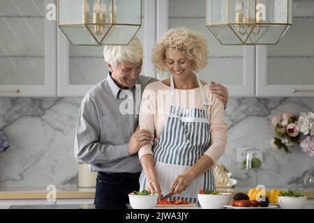 Felice marito anziano abbracciando moglie in grembiule con gratitudine Foto Stock