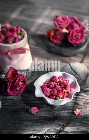 su un tavolo di legno c'è un vaso rosa con tè di rosebud. Tempo del tè, atmosfera accogliente. Cucina ancora vita con tè floreale rosa sullo sfondo del contr Foto Stock