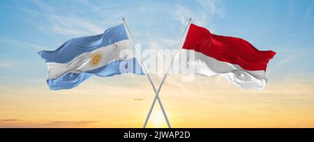 Bandiere nazionali incrociate argentine e monegasche sventolano nel vento a cielo nuvoloso. Simboleggiare relazioni, dialogo, viaggiare tra due paesi. Foto Stock