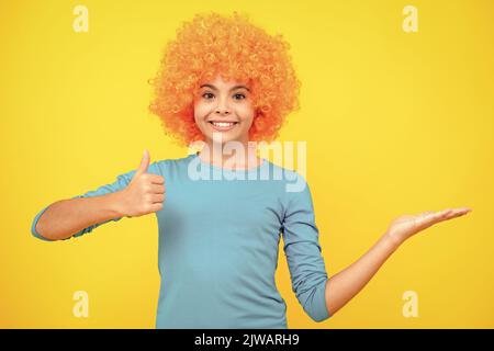 Bella ragazza adolescente in parrucca isolato sul giallo. Divertente clown wig. Buon ritratto adolescente. Ragazza sorridente. Foto Stock