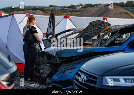 Duisburg, Germania. 04th Set, 2022. Un poliziotto si erge tra i veicoli bruciati in un parcheggio fuori dalla tenda del circo FlicFlac dopo che un piccolo aereo si è schiantato lì. Due persone sono state uccise quando l'aereo ultraleggero si è schiantato vicino all'autostrada A59 vicino a Duisburg. Il relitto è stato nascosto con schermi di privacy. Credit: Christoph Reichwein/dpa/Alamy Live News Foto Stock