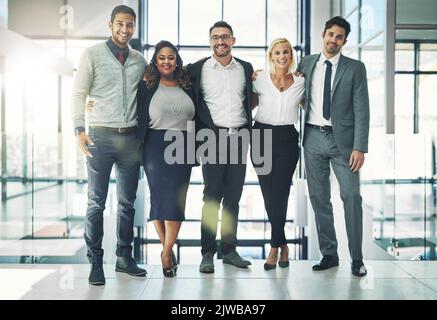 Collaborare è stata una mossa intelligente. Ritratto di un gruppo eterogeneo di colleghi sorridenti in piedi braccio in un ufficio. Foto Stock
