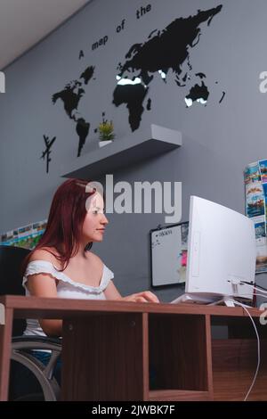 Donna che lavora al suo computer in un'agenzia di viaggi con una mappa sullo sfondo. Agente di viaggio nel suo ufficio. Foto di alta qualità Foto Stock