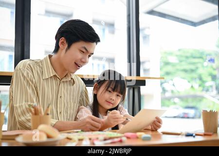 Felice e sorridente giovane figlia asiatica sta godendo un laboratorio di pittura con suo padre. Famiglia felice e attività creativa hobby per i bambini concetto Foto Stock