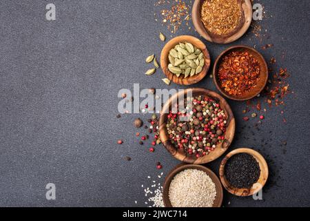 Vista dall'alto di spezie o condimenti in piccole ciotole di legno come ingrediente per alimenti sani su fondo di cemento nero Foto Stock