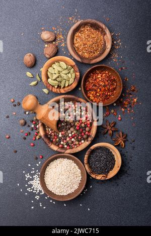 Vista dall'alto di spezie o condimenti in piccole ciotole di legno come ingrediente per alimenti sani su fondo di cemento nero Foto Stock