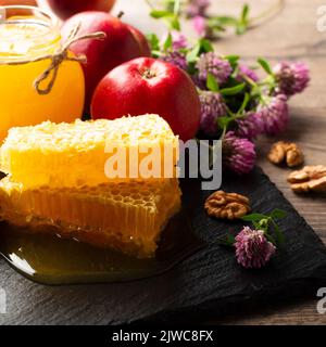 Vaso Mason con miele, nido d'ape, mele rosse e noci sul tavolo da cucina Foto Stock