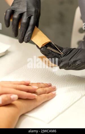 Il maestro di manicure prende gli attrezzi di manicure da una busta di kraft in un salone delle unghie Foto Stock