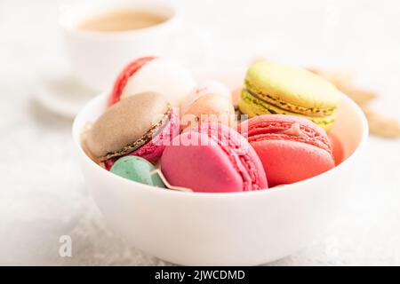Macaroni multicolore e uova di cioccolato in ciotola di ceramica, tazza di caffè su fondo grigio di cemento. Vista laterale, primo piano, fuoco selettivo, vita morta Foto Stock