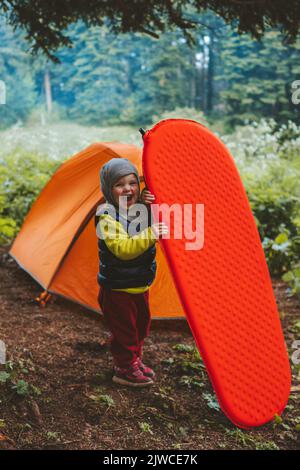 Famiglia campeggio bambino con cuscino e tenda attrezzatura viaggio avventura vacanze attrezzatura escursionistica all'aperto in foresta sano stile di vita Foto Stock