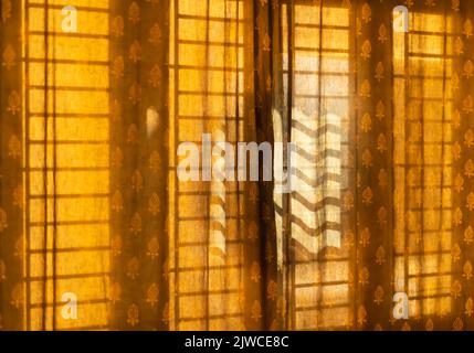 Il sole del mattino proietta un'ombra della griglia della finestra / griglia su una tenda. Foto Stock