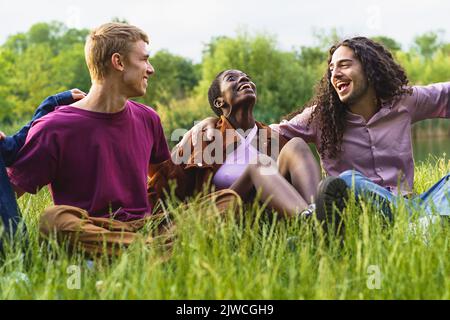Allegri amici multietnici che si legano e si divertono abbracciando e ridendo sull'erba divertirsi insieme - Gruppo di allegri multirazziali gen z giovani Foto Stock
