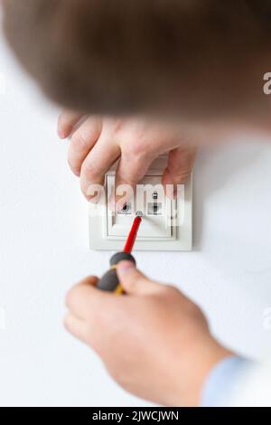 Installazione del primo piano del socket. L'elettricista stringe a mano i bulloni nel dispositivo di fissaggio a parete o nella presa utilizzando un cacciavite. L'elettricista esegue lavori elettrici a casa Foto Stock