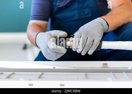 Strumento di refrigerazione. Il tecnico maschile prepara gli attrezzi per collegare rapidamente il tubo flessibile di raffreddamento al condizionatore d'aria. Primo piano delle mani maschili in guanti protettivi hol Foto Stock