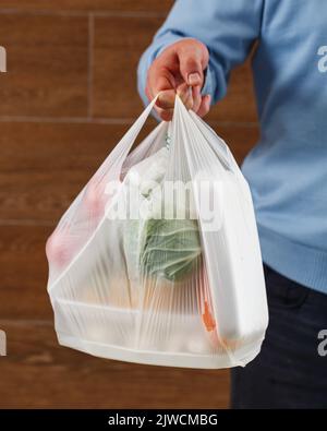 Primo piano del sacchetto di plastica trasparente bianco con il cibo in mano a un uomo sconosciuto. Foto Stock